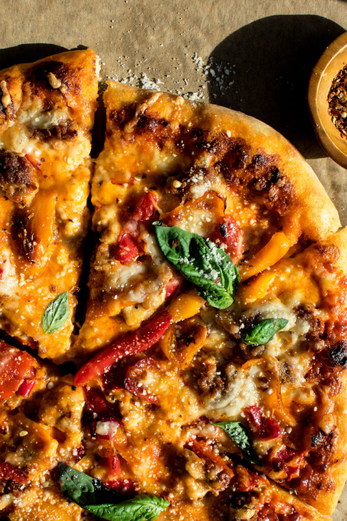 sausage & sweet pepper pizza sliced and topped with fresh basil