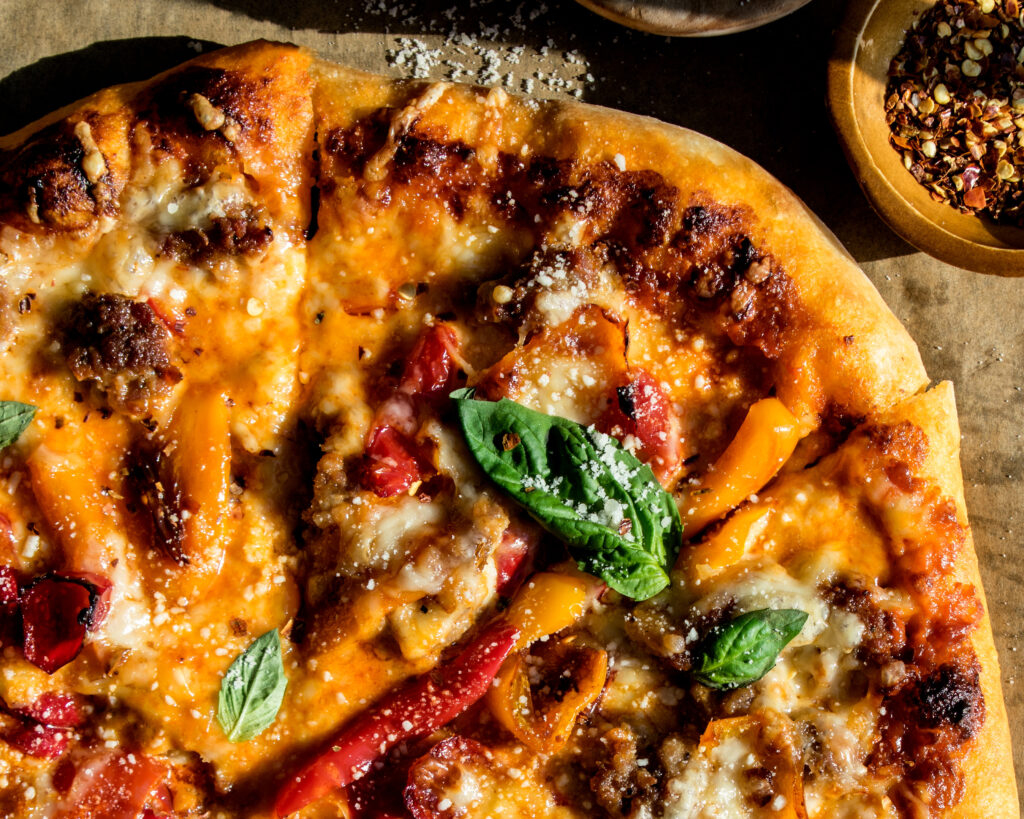 sausage & sweet pepper pizza sliced and topped with fresh basil