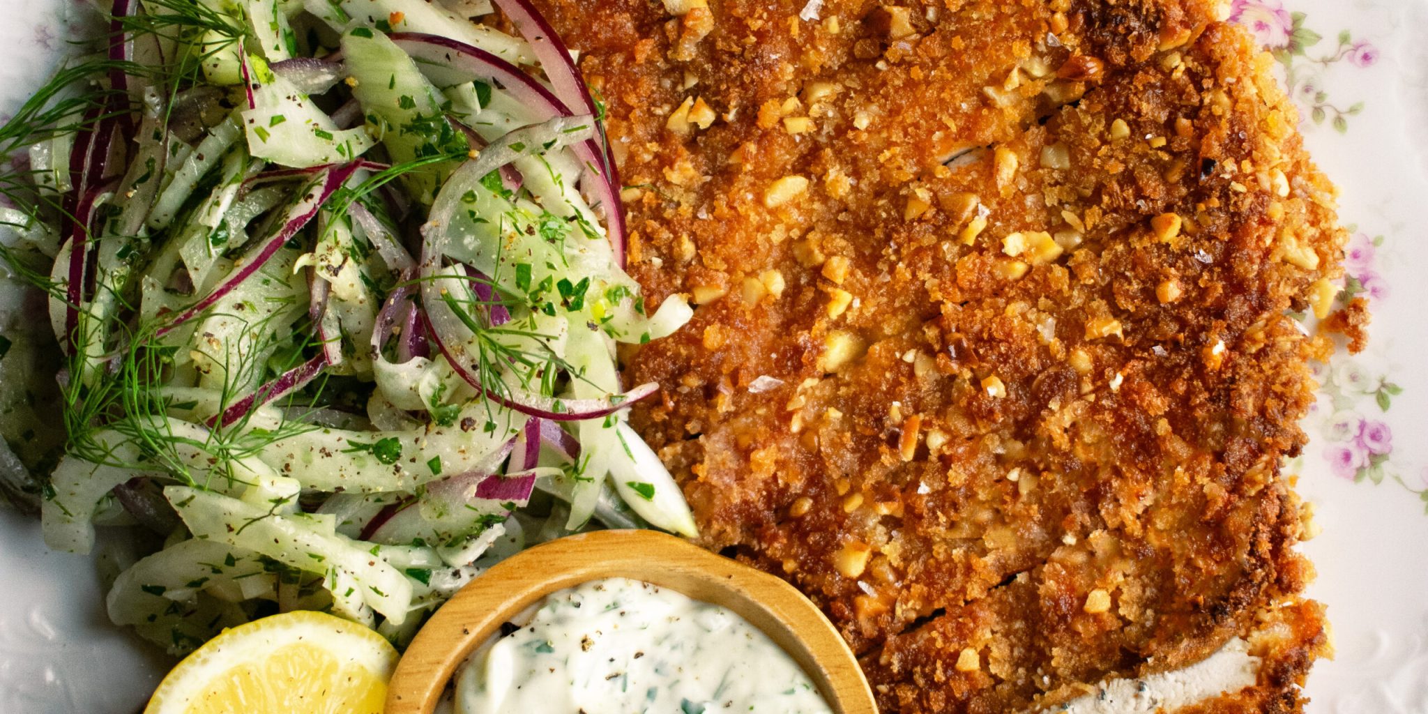 plate of sliced walnut crusted chicken, fennel slaw, herb mayo, and a lemon half
